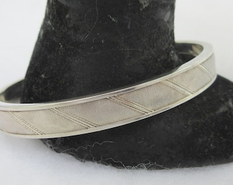 May include: A silver bangle bracelet with a textured, diagonal pattern.