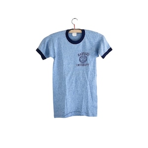 May include: A light blue t-shirt with a navy blue ringer and a navy blue Harvard University logo on the front.