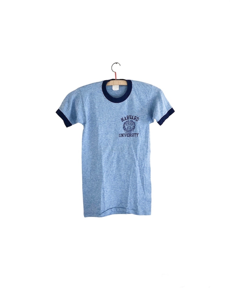 May include: A light blue t-shirt with a navy blue ringer and a navy blue Harvard University logo on the front.