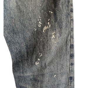 Puede incluir: Primer plano de un par de pantalones vaqueros azules con salpicaduras de pintura blanca.