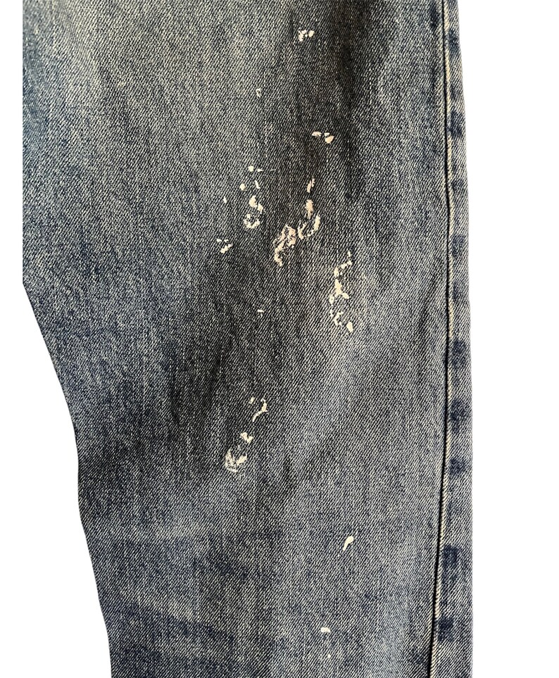 Puede incluir: Primer plano de un par de pantalones vaqueros azules con salpicaduras de pintura blanca.