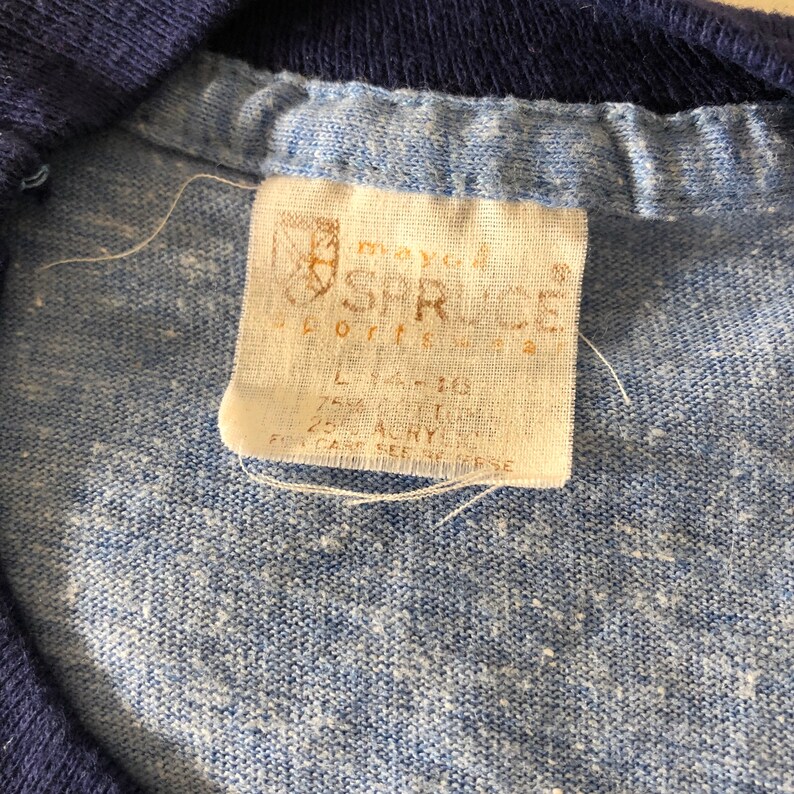 May include: A white tag with the text "SHRICE Sportswear" and size information. The tag is attached to a blue and white shirt.