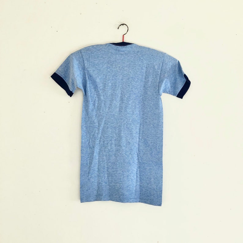 May include: A light blue t-shirt with a dark blue contrast trim on the collar and sleeves.