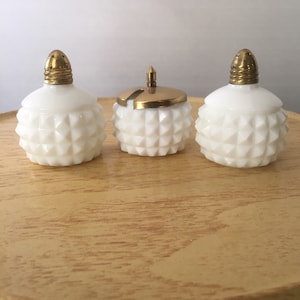 Peut inclure: Ensemble de trois salières et poivrières blanches avec des dessus dorés. Les salières ont un motif en forme de diamant.