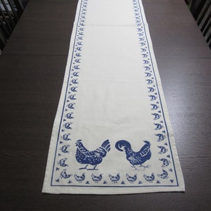 May include: A white table runner with a blue and white chicken design. The runner has a border of blue chickens on each side.