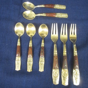 May include: A set of vintage cutlery, including spoons and forks, displayed on a blue background. The utensils have brass heads and decorative details, with dark wood handles. The spoons and forks are in different sizes.