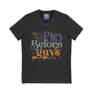 May include: Dark gray v-neck t-shirt with the phrase "Pies Before Guys" in a retro font. The design includes a pizza slice graphic and star accents. The shirt has a tag that says "Kirby Grace Co."
