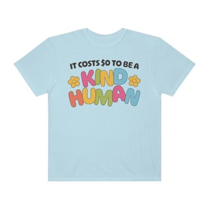 Peut inclure: T-shirt bleu clair avec le texte "Il en coûte 0 € pour être un être humain bienveillant" en lettres colorées avec des visages souriants.