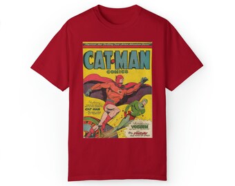 Può includere: Maglietta rossa con una copertina di fumetto vintage che presenta un supereroe chiamato "Cat-Man Comics". La copertina mostra un supereroe rosso e giallo che vola nell'aria con un cattivo verde sullo sfondo.