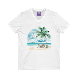 Pode incluir: Camiseta branca de gola em V com uma ilustração em aquarela de uma cena de praia. A ilustração apresenta uma palmeira, duas espreguiçadeiras, um guarda-sol e o texto "São 5 horas em algum lugar".