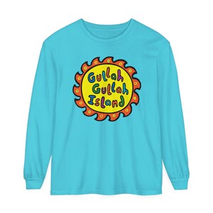 Może przedstawiać: Turkusowy t-shirt z długim rękawem z grafiką żółtego słońca. Słońce ma czerwony kontur, a słowa "Gullah Gullah Island" są napisane kolorowymi literami.