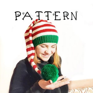 May include: A red and white striped knitted hat with a long green and white striped tail. The hat has a green pom pom on the end of the tail.