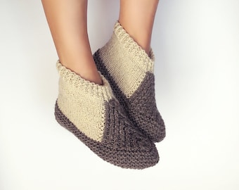 Può includere: Un paio di calzini da pantofola in maglia beige e marrone. I calzini sono realizzati con un motivo a treccia e hanno una punta a punta.