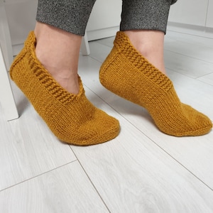 May include: A pair of mustard yellow knitted slipper socks. The socks are made of a soft, cosy material and have a comfortable fit.