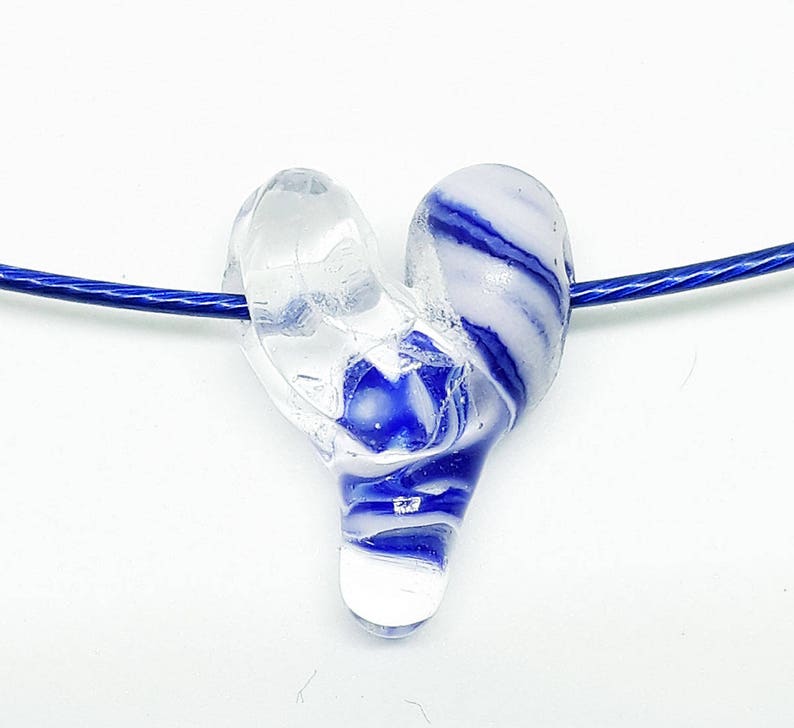 May include: A blue and white glass heart pendant on a blue cord necklace. The heart is made of clear glass with blue and white swirls.