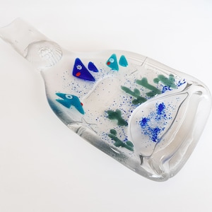 May include: A clear glass bottle shaped dish with a blue, green and red mosaic design. The dish is decorated with small glass fish and sea life.