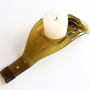 May include: A green glass candle holder shaped like a wine bottle, with a white candle and red and gold accents.