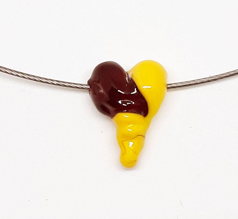 May include: A heart-shaped pendant necklace with a yellow and maroon glass bead. The bead is shaped like a heart with a swirl design.