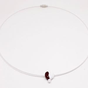 May include: A silver necklace with a clear cord and a heart-shaped pendant. The pendant is half white and half burgundy.
