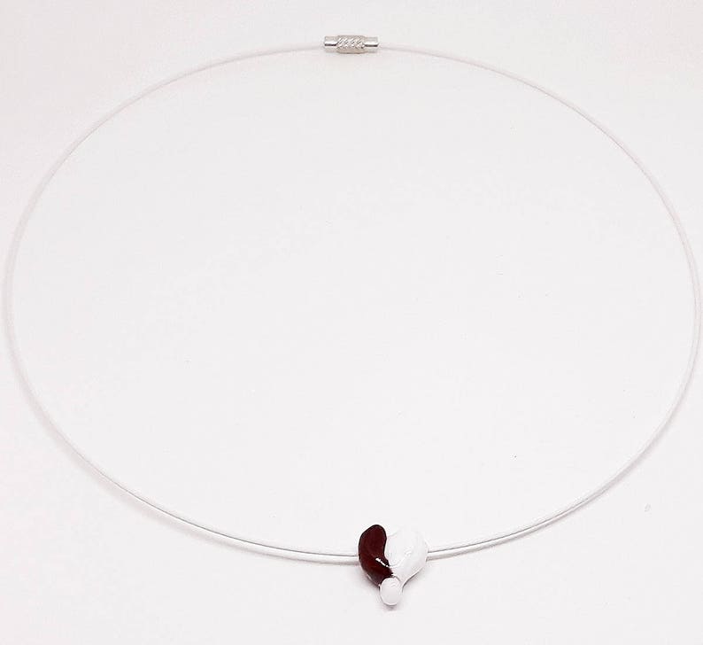 May include: A silver necklace with a clear cord and a heart-shaped pendant. The pendant is half white and half burgundy.