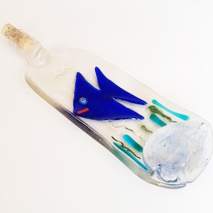 May include: A clear glass bottle with a blue fish and green seaweed design. The bottle has a cork stopper and is a decorative piece.