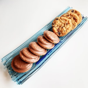 Könnte beinhalten: Ein blaues Glasserviertablett mit verschiedenen Schokoladenüberzogenen Keksen und Schokoladen-Chip-Keksen. Die Kekse sind in einer Reihe auf dem Tablett angeordnet.