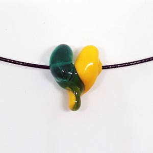 May include: A green and yellow glass heart pendant on a black cord necklace.