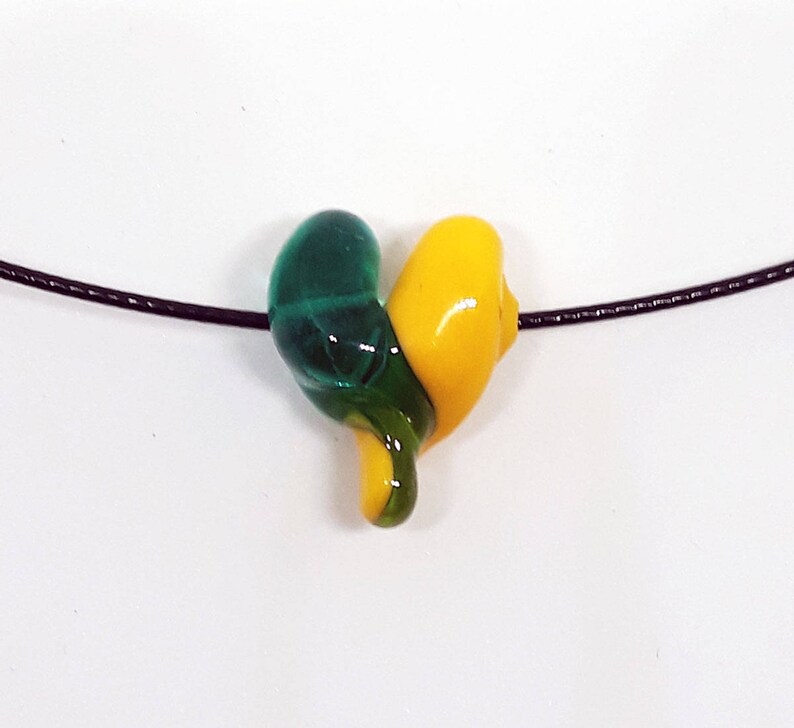 May include: A green and yellow glass heart pendant on a black cord necklace.