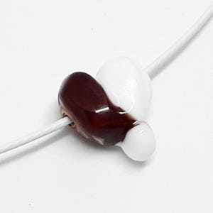 May include: A white and brown heart-shaped glass bead on a white string.