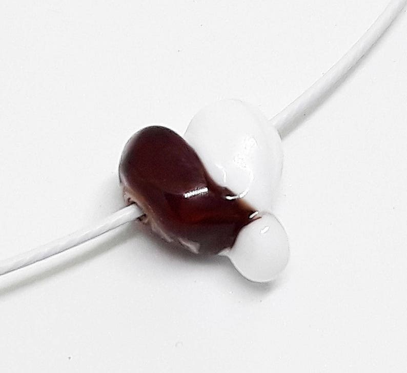 May include: A white and brown heart-shaped glass bead on a white string.