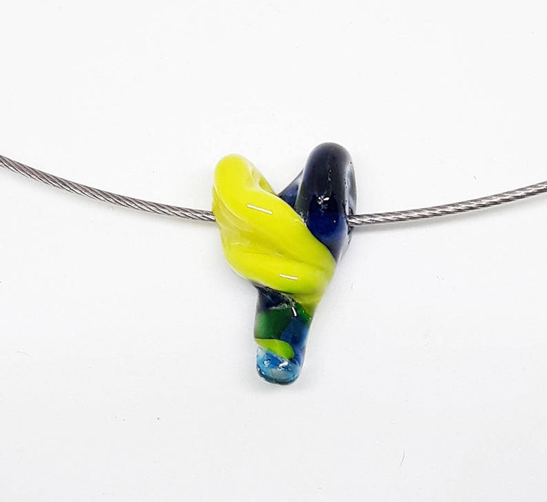 May include: A yellow, blue, and green glass pendant hangs from a silver chain. The pendant is shaped like a swirl or a knot.