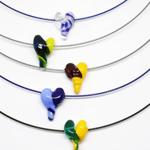 May include: Five glass heart necklaces on thin silver chains. The hearts are in various colors, including blue, green, yellow, and brown.