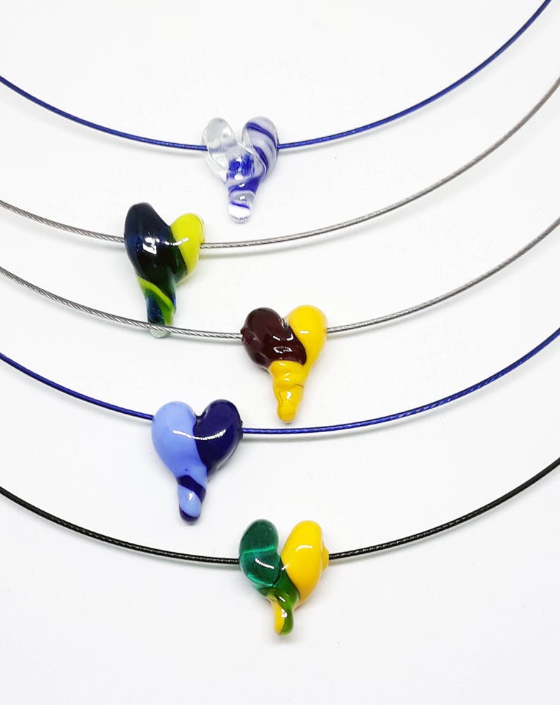 May include: Five glass heart necklaces on thin silver chains. The hearts are in various colors, including blue, green, yellow, and brown.