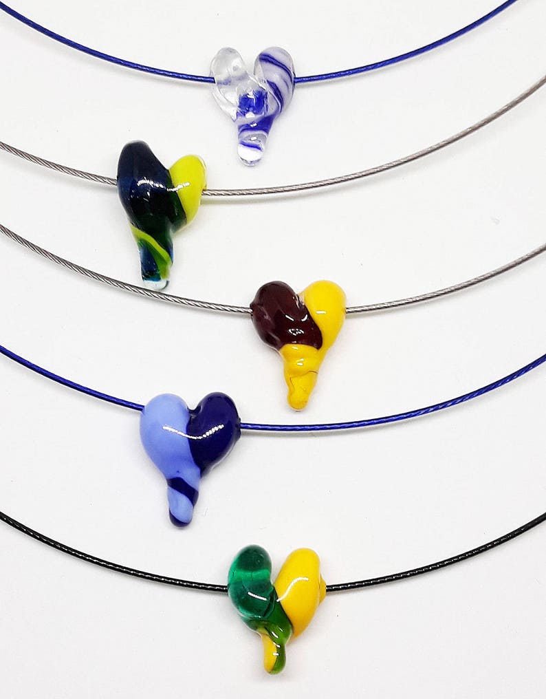 May include: Five necklaces with different colored glass heart pendants. The hearts are all in a swirl pattern and are made of clear, blue, green, yellow, and brown glass.