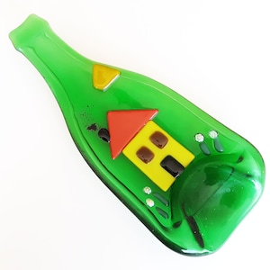 May include: A green glass bottle with a yellow and red house design. The bottle is shaped like a wine bottle and has a small indentation on the side.