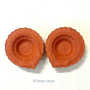 Pode incluir: Duas l&acirc;mpadas de &oacute;leo decorativas de cor terracota. Cada l&acirc;mpada apresenta uma borda ondulada e padr&otilde;es em relevo intrincados, incluindo um design floral central e motivos laterais detalhados. As l&acirc;mpadas s&atilde;o projetadas para conter &oacute;leo e um pavio.