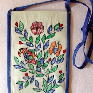 May include: A rectangular off-white crossbody bag featuring a hand-drawn illustration of a bird, a butterfly, and a large flower surrounded by green and blue leaves. The bag has blue fabric trim and a matching blue shoulder strap. Text reads Store Utsav.