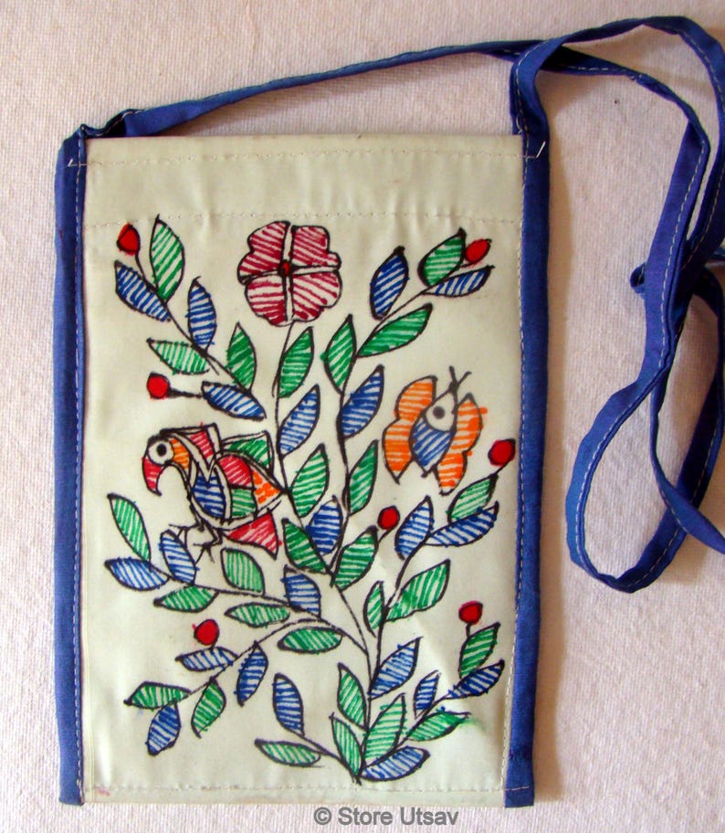 May include: A rectangular off-white crossbody bag featuring a hand-drawn illustration of a bird, a butterfly, and a large flower surrounded by green and blue leaves. The bag has blue fabric trim and a matching blue shoulder strap. Text reads Store Utsav.
