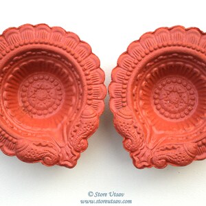Pode incluir: Duas l&acirc;mpadas a &oacute;leo cor de terracota com intrincados padr&otilde;es florais e geom&eacute;tricos. As l&acirc;mpadas t&ecirc;m uma borda ondulada e um design central. A imagem &eacute; tirada de cima, mostrando os detalhes das l&acirc;mpadas em um fundo branco.