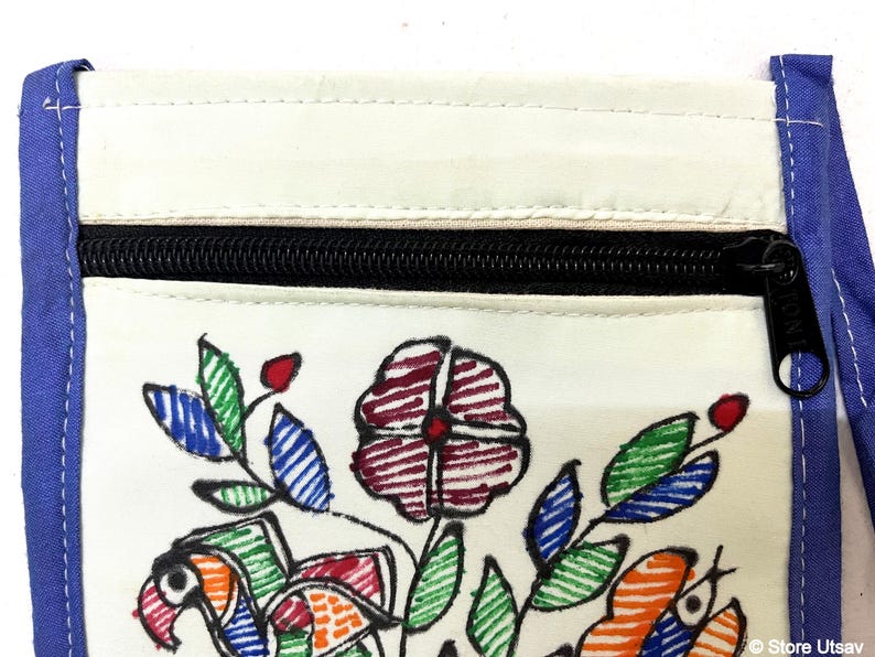 May include: A cream-colored fabric pouch featuring a hand-drawn floral and bird design in red, green, blue, and orange ink. The pouch has a black zippered closure at the top and is bordered by blue fabric trim along the sides and top edges.