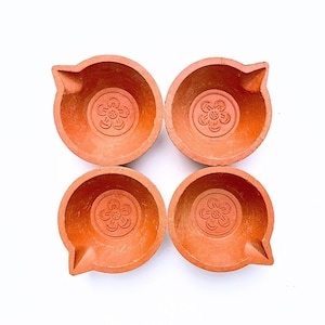 Four terracotta diya lamps with a floral design. The diyas are a traditional Indian lamp used during festivals like Diwali. Authentic Handmade Clay Diyas by Store Utsav. Global shipping.