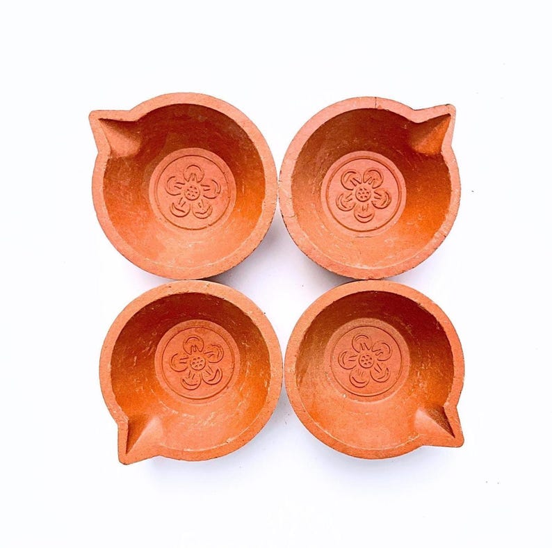 Four terracotta diya lamps with a floral design. The diyas are a traditional Indian lamp used during festivals like Diwali. Authentic Handmade Clay Diyas by Store Utsav. Global shipping.