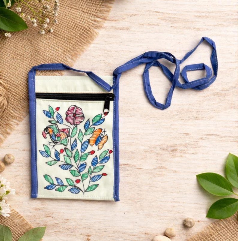 Front view of a mint upcycled cotton zippered pouch with a blue trim extending to form a long blue strap by Store Utsav. The pouch has Madhubani painting done. Its a floral design with green leaves, red flowers, and orange and blue birds. The pouch is a great way to carry your phone, keys, or other small items. Global shipping!