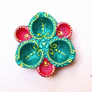 May include: A multi-compartment oil lamp shaped like a flower with three large teal sections and two smaller red sections. The teal sections feature intricate embossed patterns and yellow painted outlines, while the red sections have ribbed textures.