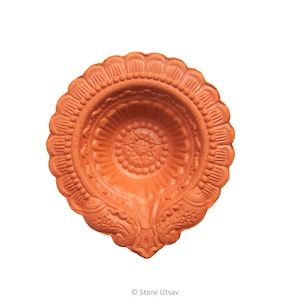 以下が含まれることがあります： 複雑な花柄が施された、伝統的なインドの油ランプであるテラコッタ製のディーヤ。ディーヤはハート型で、油と芯を入れるための丸い中心部があります。