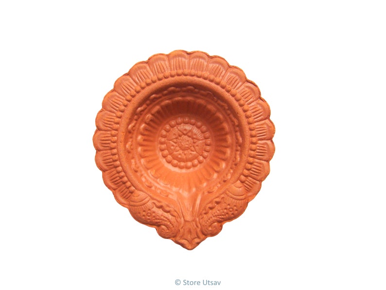 Pode incluir: Uma diya de terracota, uma l&acirc;mpada de &oacute;leo tradicional, com intrincados padr&otilde;es florais e geom&eacute;tricos. A l&acirc;mpada tem uma borda ondulada e um po&ccedil;o central para &oacute;leo e um pavio. A diya &eacute; de cor castanho-alaranjada quente, sobre fundo branco.