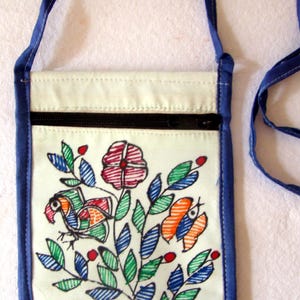 May include: A rectangular off-white fabric crossbody bag with a blue trim and strap. The front features a hand-drawn style illustration of a bird, a flower, and a butterfly in red, green, and blue ink. A black zipper runs across the top section.