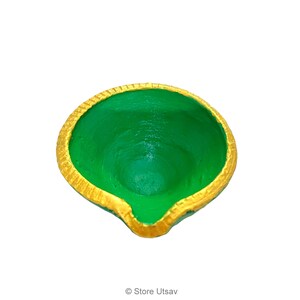 May include: A small, round, bowl-shaped diya oil lamp featuring a vibrant green interior and a textured, metallic gold painted rim. The lamp has a distinct pointed spout at the front edge, designed for holding a wick, with a smooth, painted finish.