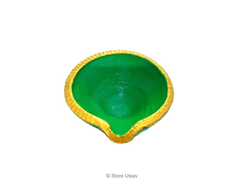 May include: A small, round, bowl-shaped diya oil lamp featuring a vibrant green interior and a textured, metallic gold painted rim. The lamp has a distinct pointed spout at the front edge, designed for holding a wick, with a smooth, painted finish.