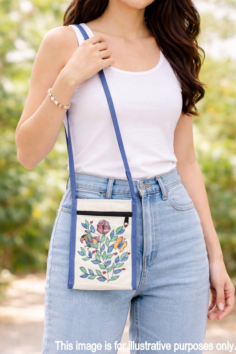 May include: A small, rectangular off-white canvas crossbody bag featuring a blue trim and a long blue shoulder strap. The front of the bag displays a colorful embroidered design of a flower, a bird, and a butterfly with green leaves.